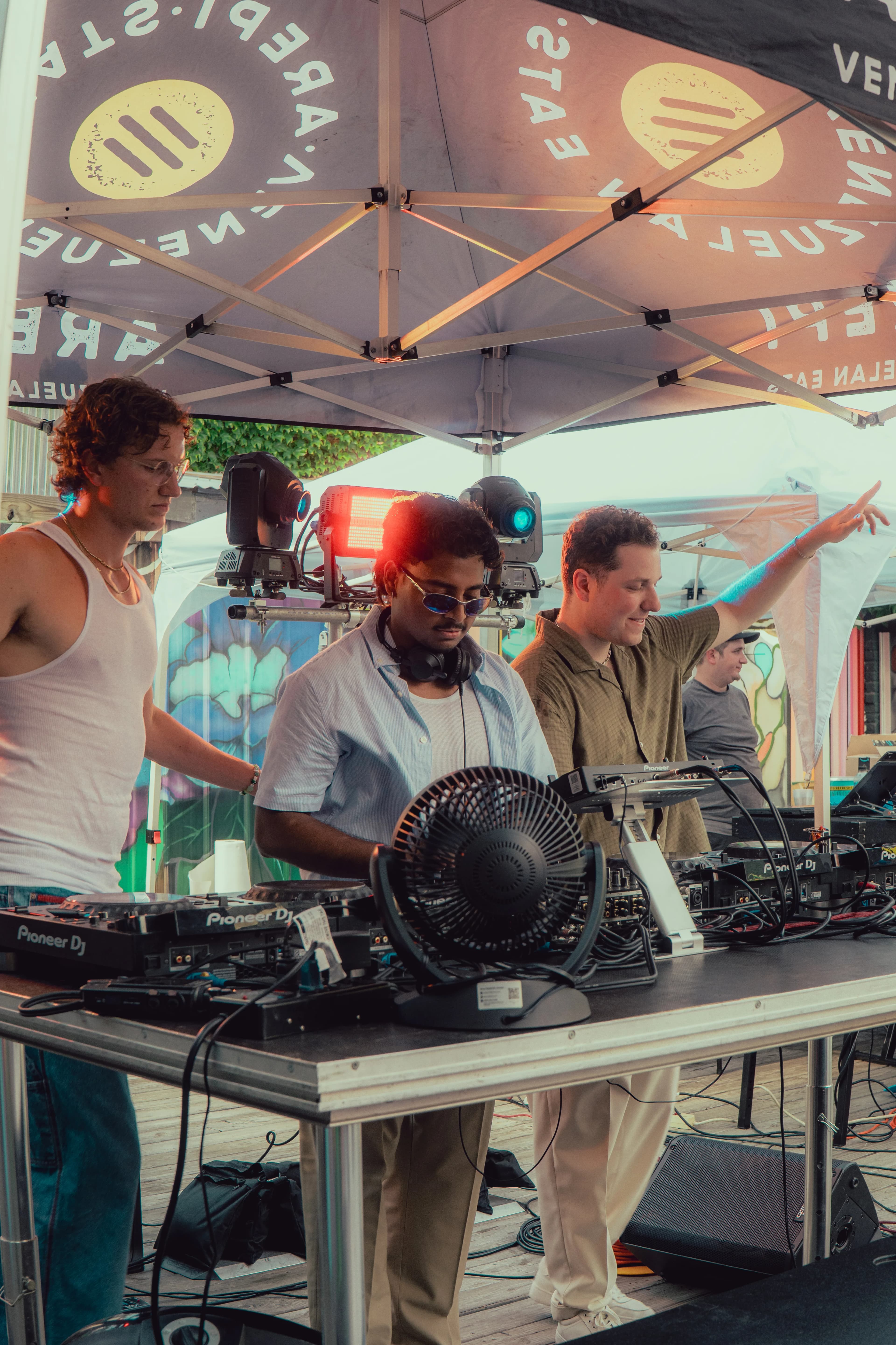 Three DJs playing under a tent outdoors